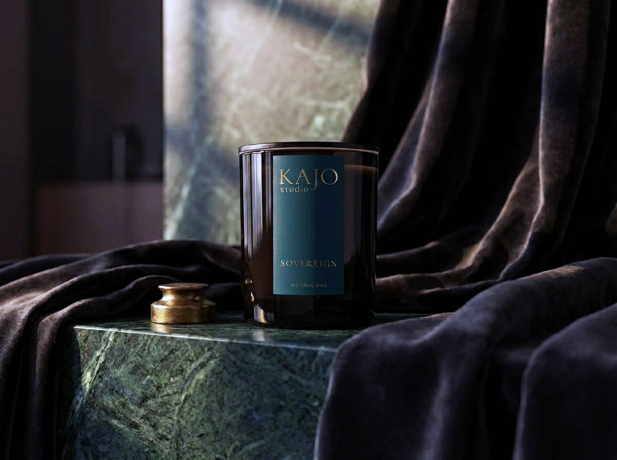 Candle with 'KAJO' branding on a marble surface with draped fabric in the background